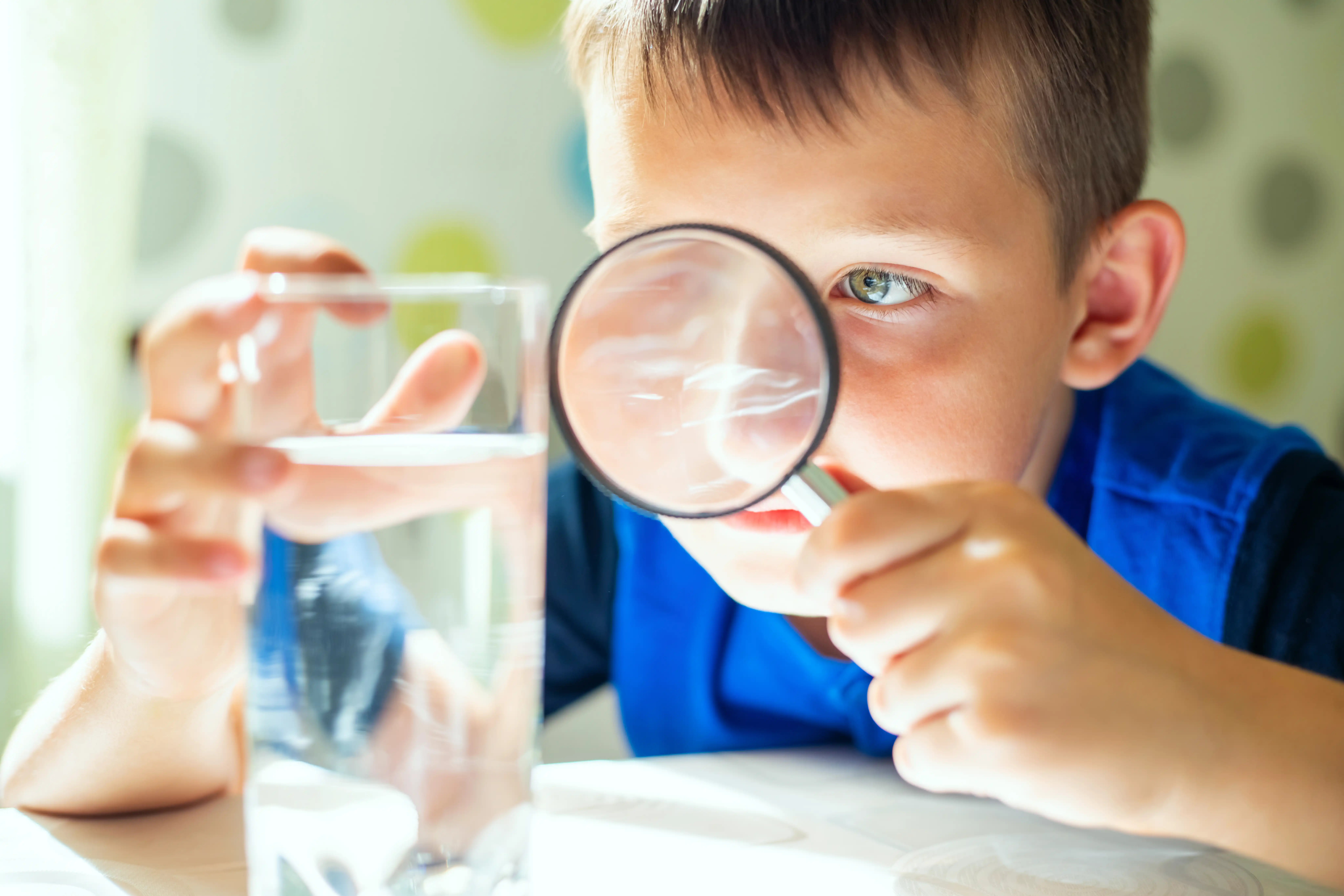 Young boy thoughtfully examining a glass of water, curious about what's inside